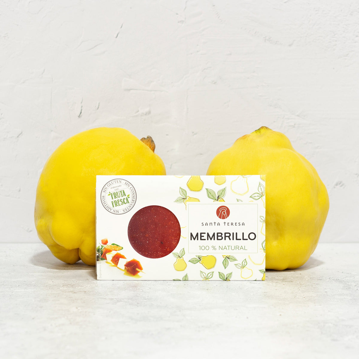 Envase de membrillo Santa Teresa de 150 g con ventana circular, junto a dos membrillos frescos